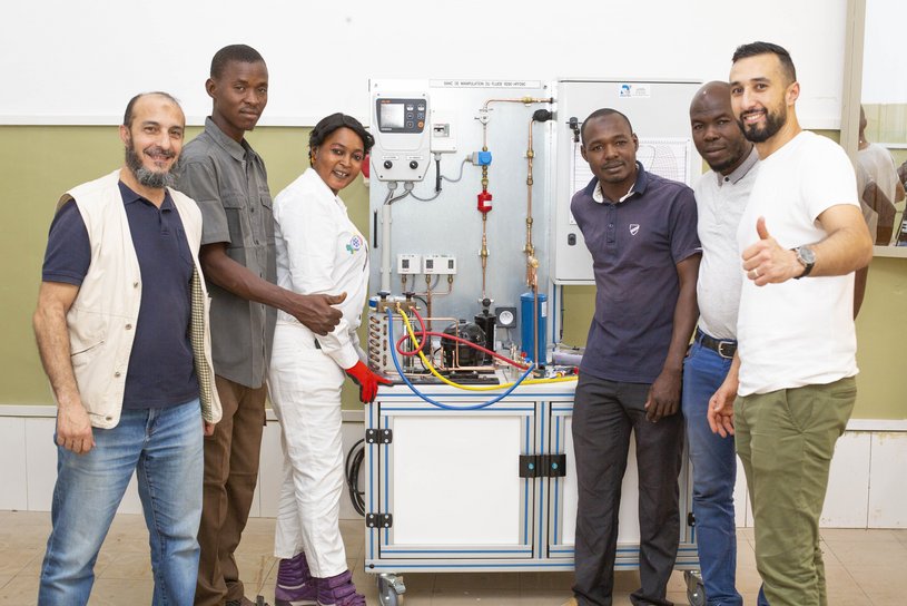 The picture shows trainers and participants in front of a training station with the model of a refrigeration cycle. (opens enlarged image)