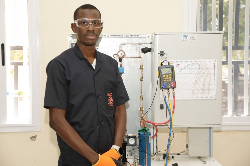 A young man with gloves and protective glasses stands in front of a training bench for natural refrigerants.